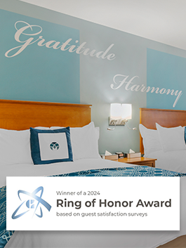 Two queen beds in a hotel room underneath the words "Gratitude" and "Harmony" painted on the wall - Winner of a 2024 Ring of Honor Award based on guest satisfaction surveys


