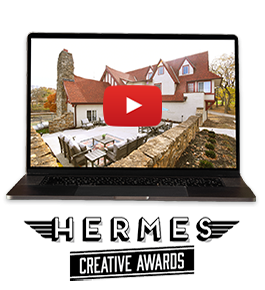 An open laptop with a video still of the Hummingbird Chateau - a large, unique, white house in Unity Village